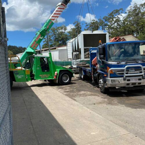 A Green Truck with A Crane Attached to It Is Being Towed by A Blue Truck — H & H Metal Recycling In Coolum, QLD