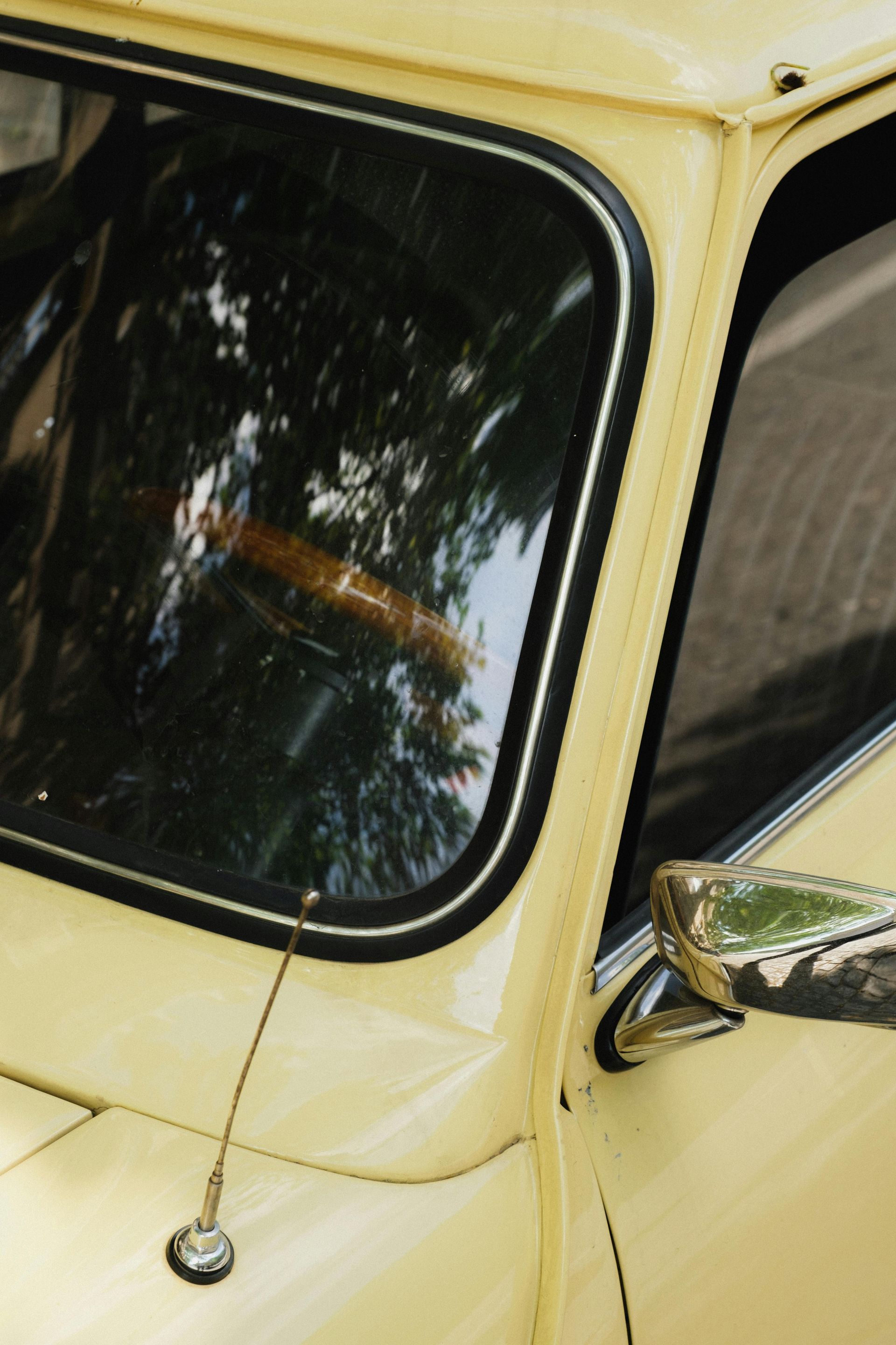 A yellow car with a reflection of trees in the window