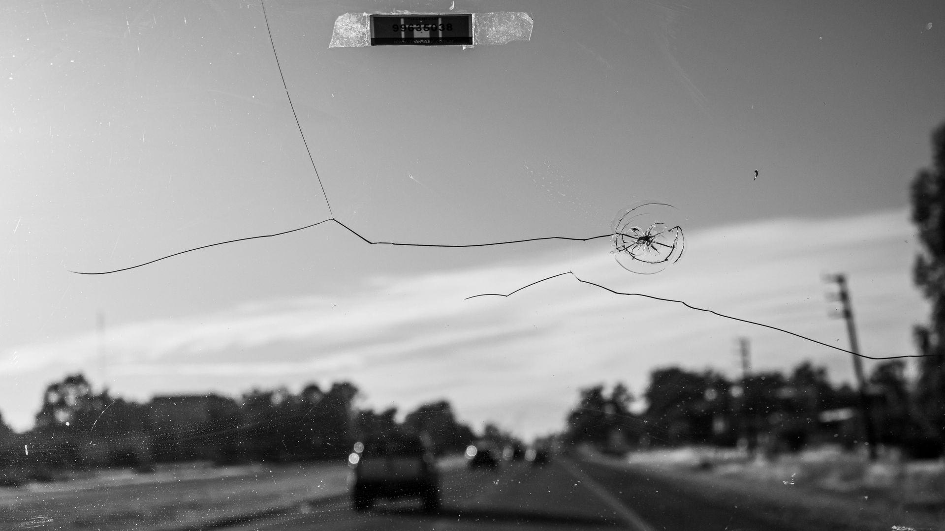 A black and white photo of a car driving down a road with a cracked windshield.