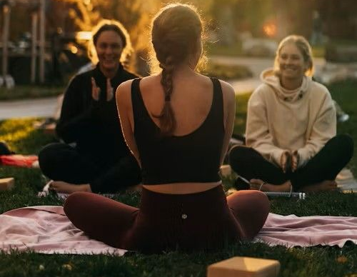 Group of people doing yoga outdoors, in the grass. One is leading with her back to the camera.