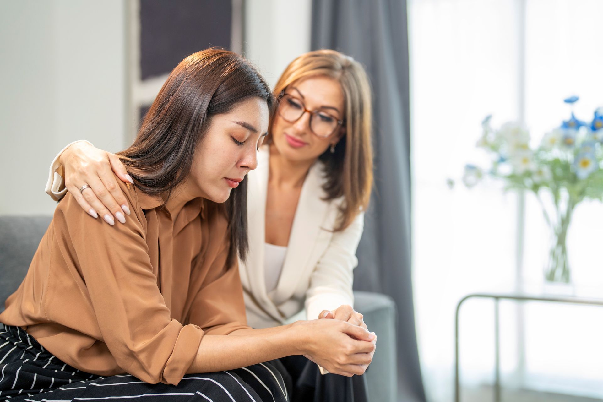Person in white blazer offers support to another seated individual in a softly lit room.