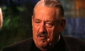 A child and a uniformed police officer stand in front of a police station with glass doors.
