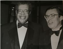 Two men in formal wear smiling, wearing bow ties and glasses.
