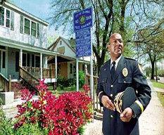 Police officer in uniform outside a police substation, holding hat, standing on a sidewalk.