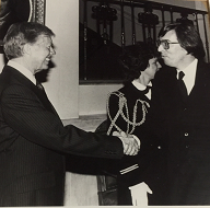 Jimmy Carter shakes hands with a man, woman in uniform between them.