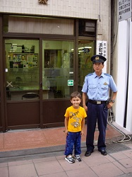 A child and a uniformed police officer stand in front of a police station with glass doors.
