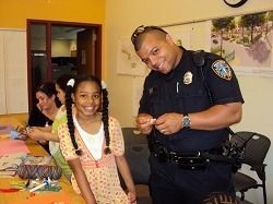 A child and a uniformed police officer stand in front of a police station with glass doors.