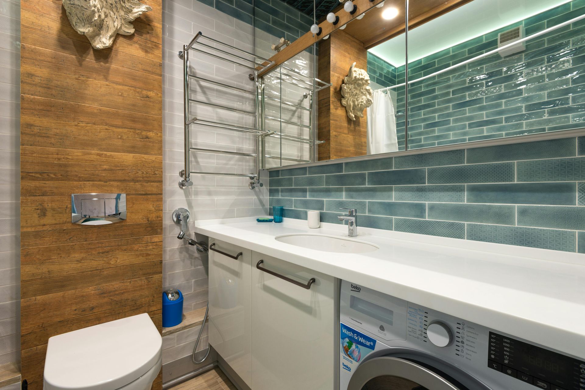 Bathroom with blue brick-like tile, a white sink, a toilet, and a washing machine under a mirror.