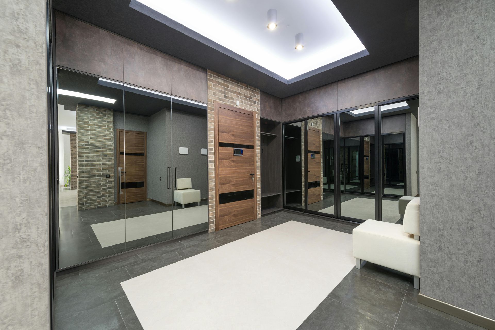 Modern hallway with mirrored closets, gray walls, white rug, and seating.