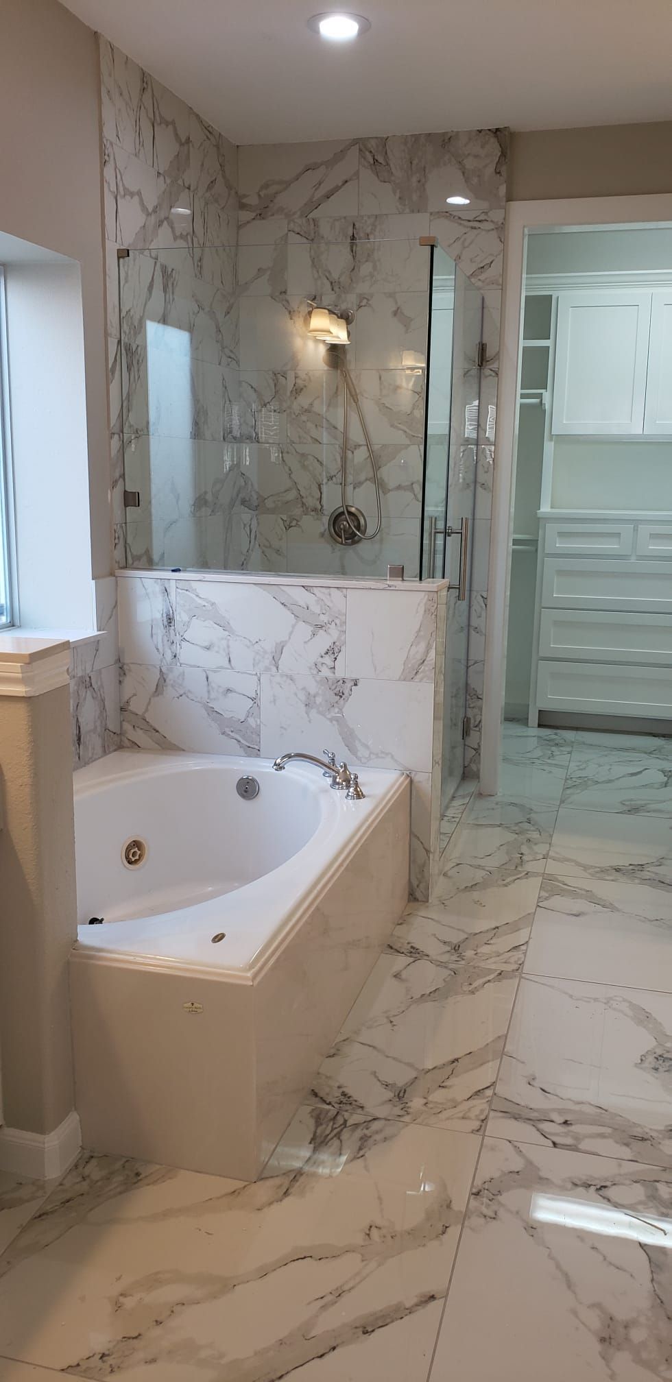 Modern bathroom with marble tile, freestanding tub, glass shower, and glossy white vanity