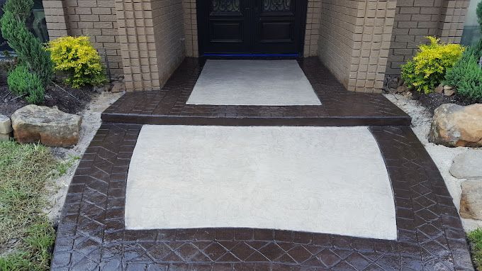 Brick walkway with two white concrete panels leading to a doorway, bordered by plants and stones