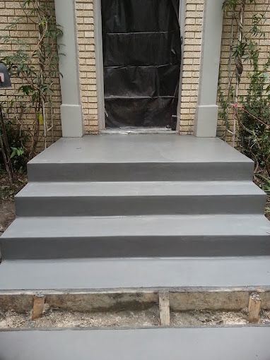Gray front steps leading to a black-covered doorway between brick walls