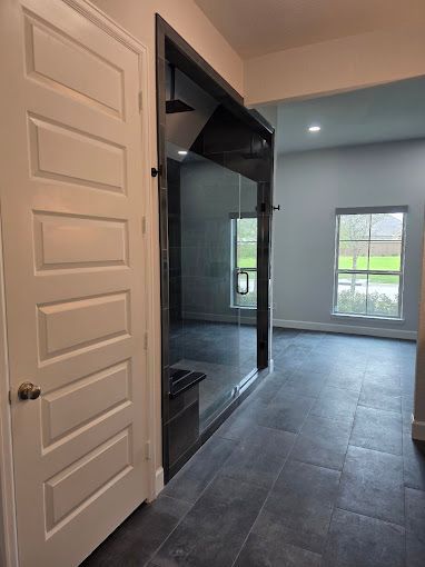 Interior hallway with dark tiled floor, open door, and a room with blue-gray walls and windows.