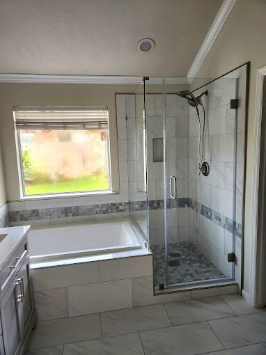 Bathroom with white tub, glass shower enclosure, tiled floor, and a window above the tub.