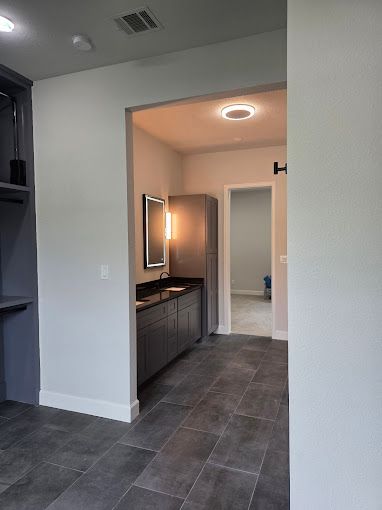 Modern bathroom with dark tile floor, double vanity, lit mirror, and open doorway to another room