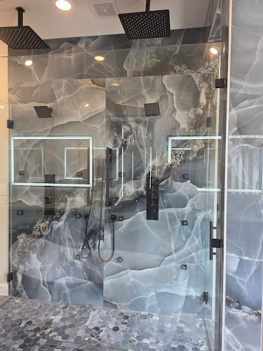 Modern bathroom with gray stone walls, glass shower enclosure, and black shower fixtures