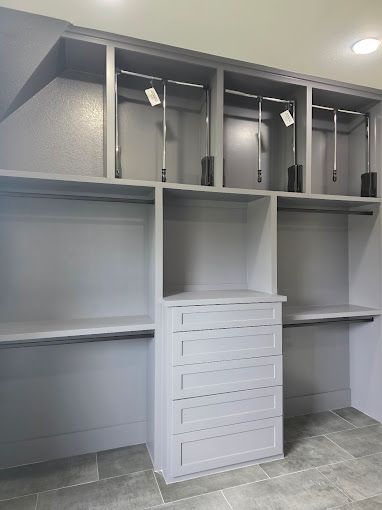 Built-in closet with shelves and hanging rods above a white dresser in a tiled room