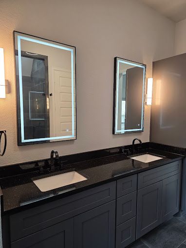 Modern bathroom vanity with two backlit mirrors, black countertop, and dual sinks