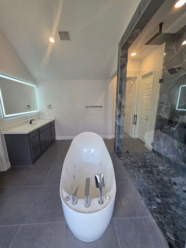 Modern bathroom with freestanding tub, vanity, shower, and gray tile flooring.