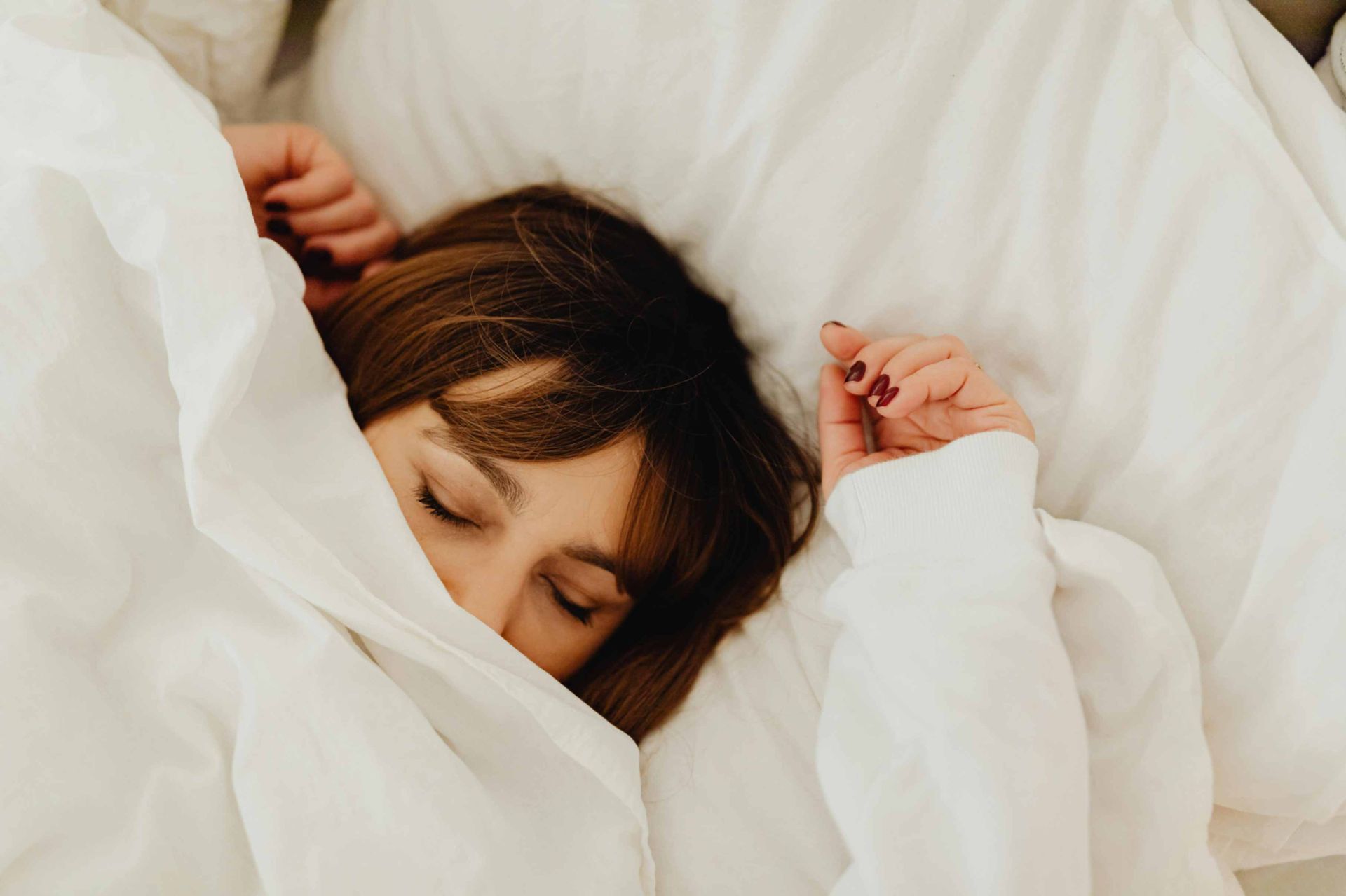 A woman is sleeping in a bed under a white blanket.