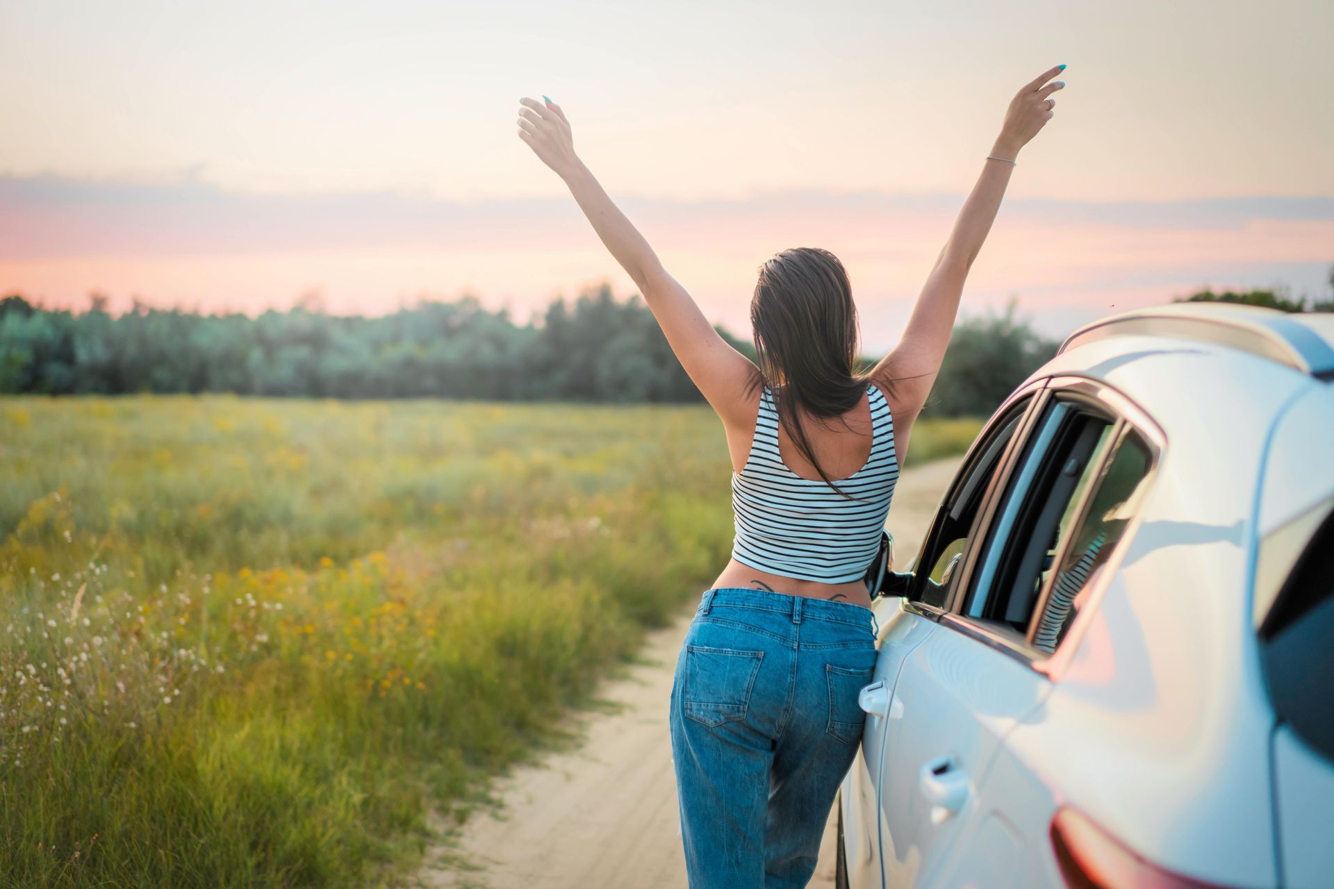 A woman is standing next to a car with her arms in the air.