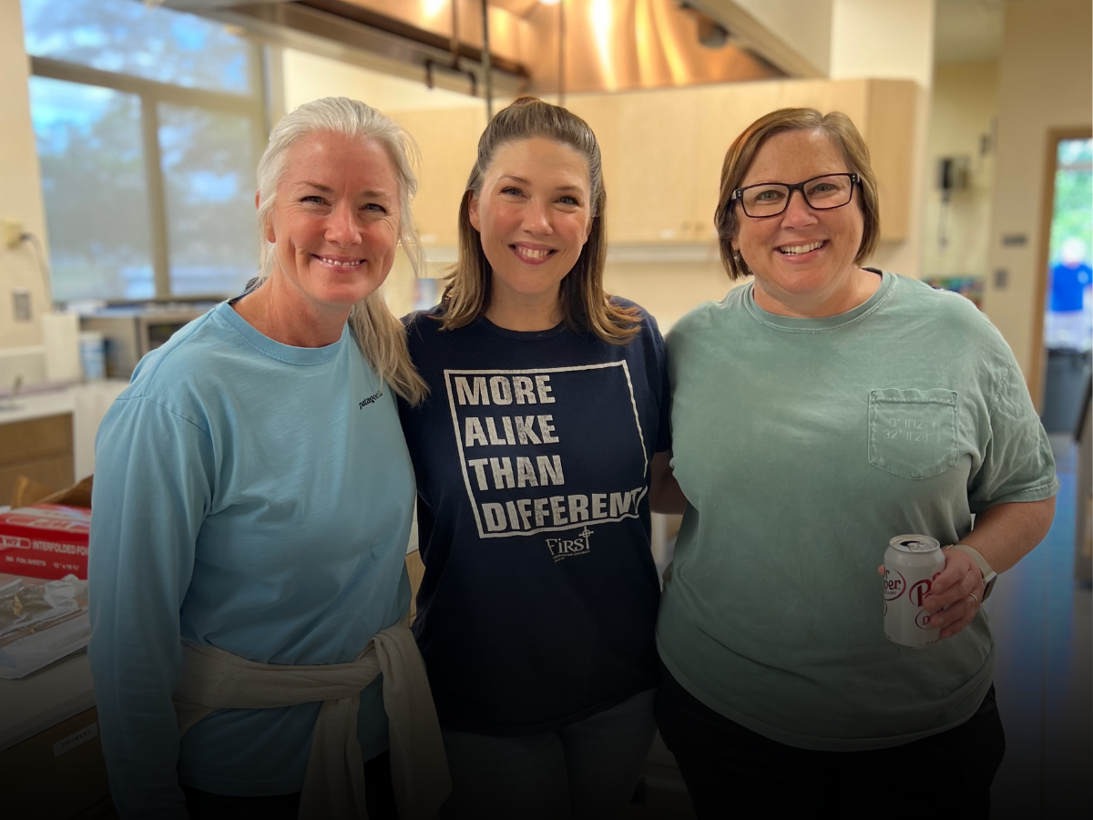 Three women are posing for a picture together in a kitchen.