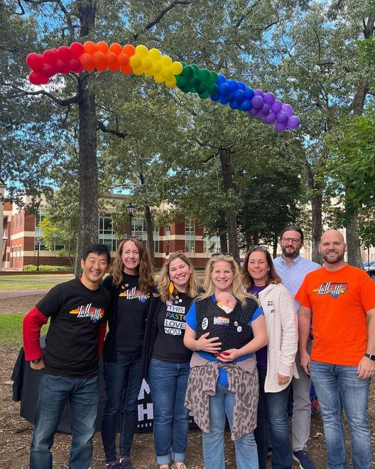 A group of people are posing for a picture in front of a rainbow balloon arch.