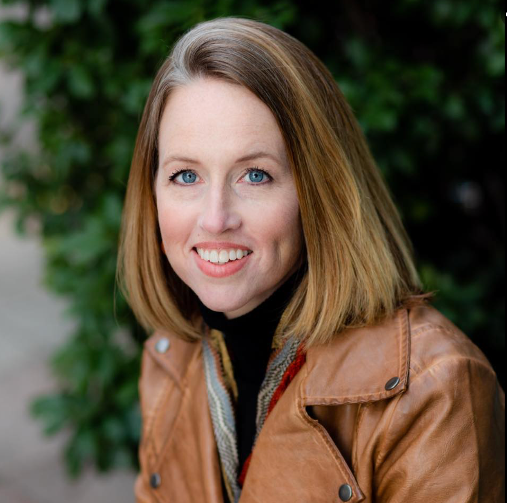 A woman in a brown leather jacket is smiling for the camera.