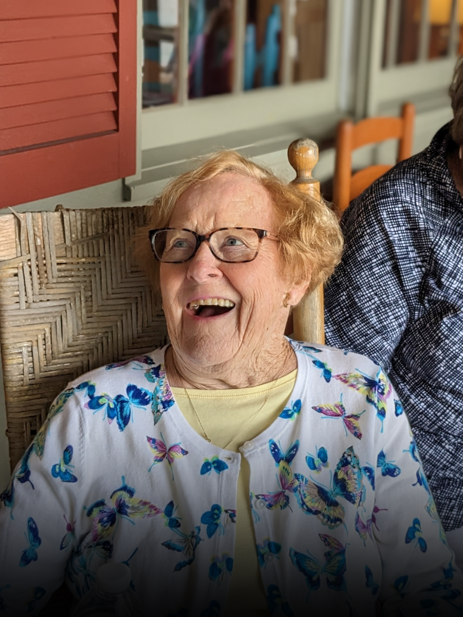 An elderly woman is sitting in a rocking chair and smiling.