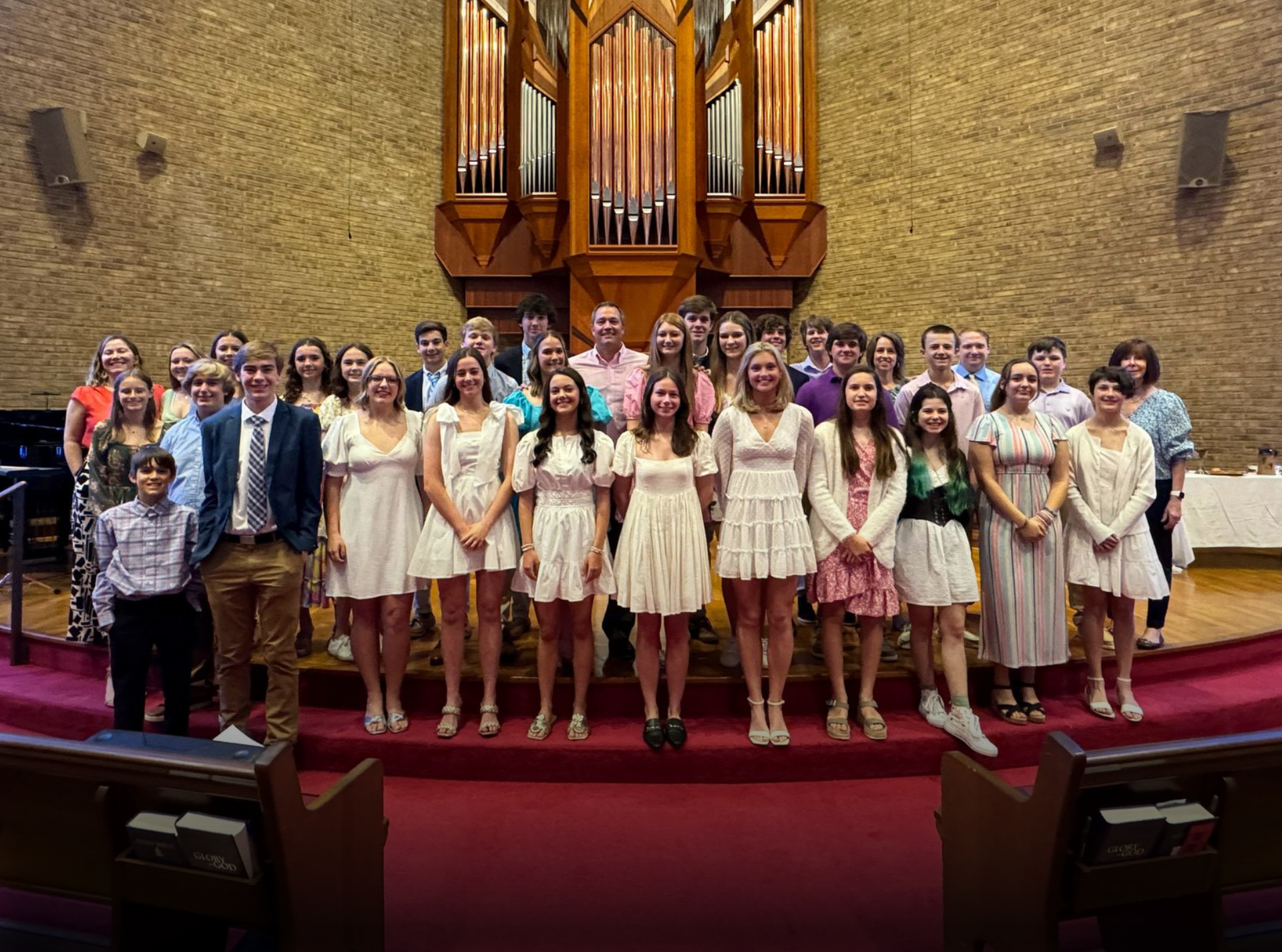 A group of people are posing for a picture in front of an organ in a church.