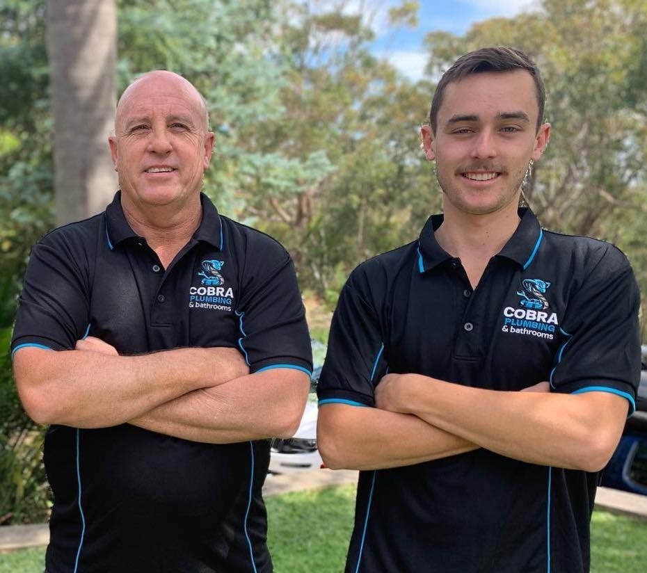 Two men with arms crossed, in black polo shirts with logo, standing outside — Cobra Plumbing & Bathrooms in Heathcote, NSW