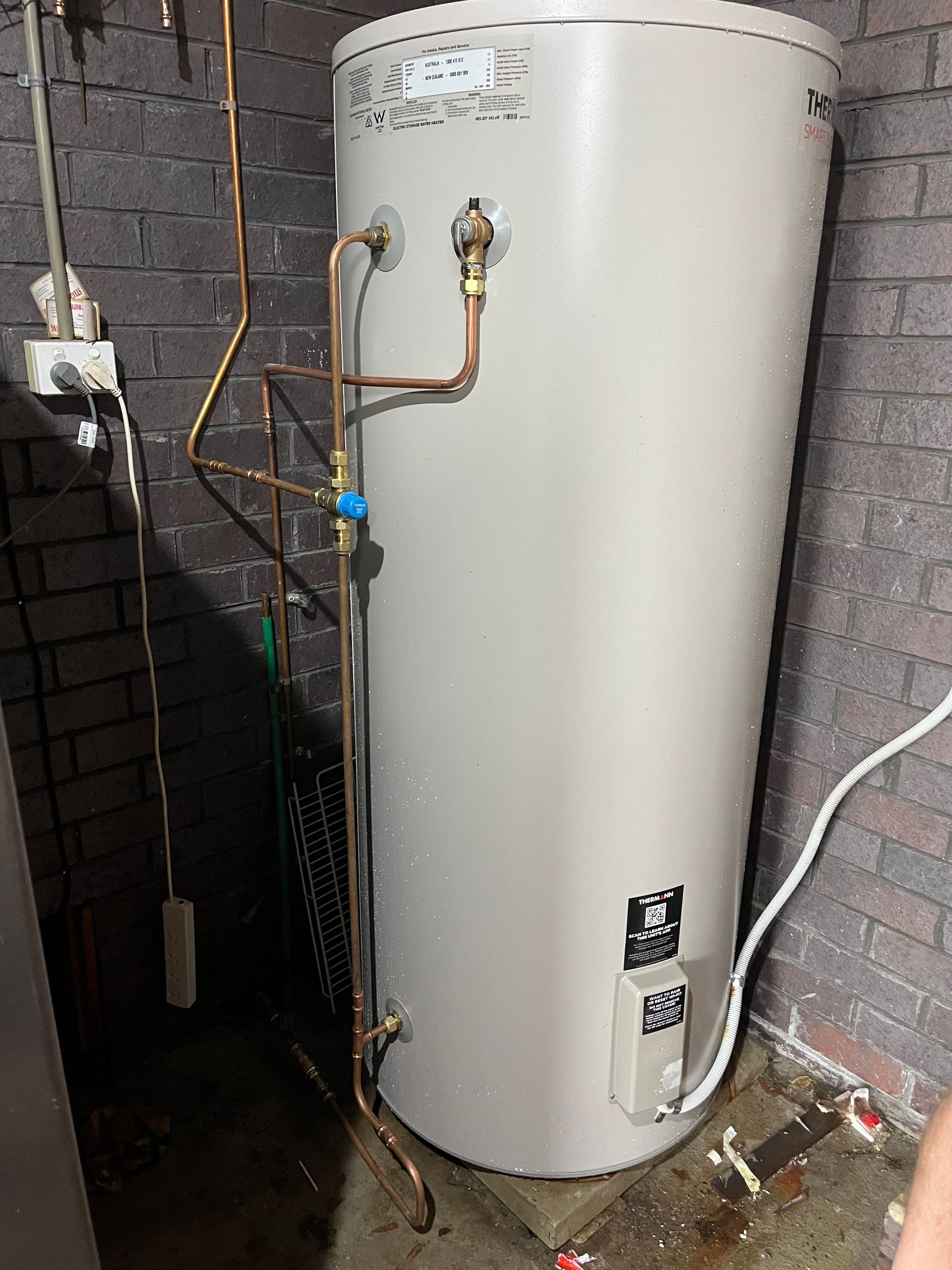 Hot water tank with copper piping in a brick-walled basement  — Cobra Plumbing & Bathrooms in Heathcote, NSW