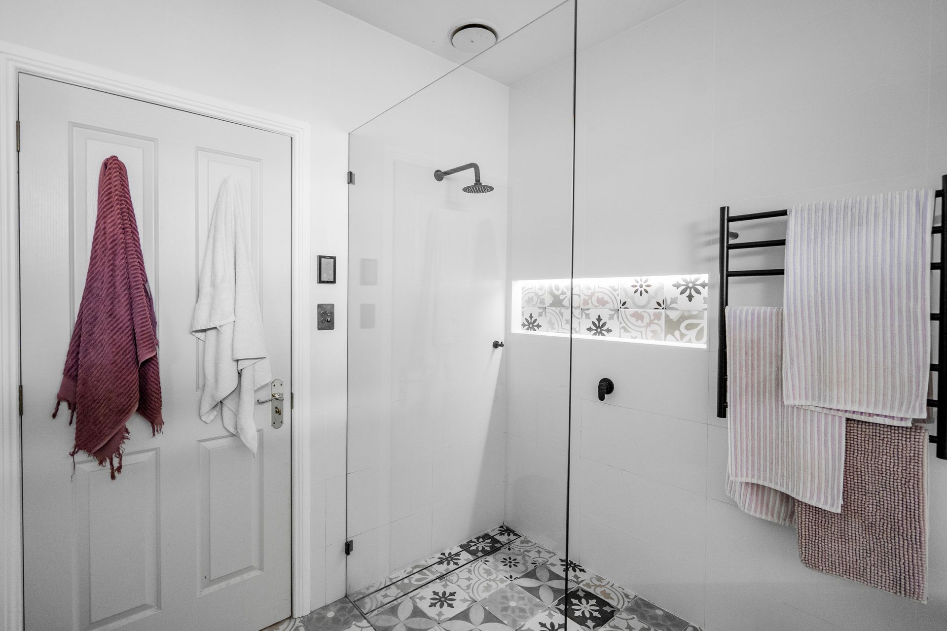 Bright white bathroom with shower, patterned tile, and towels hanging on racks and hooks — Cobra Plumbing & Bathrooms in Kiama, NSW