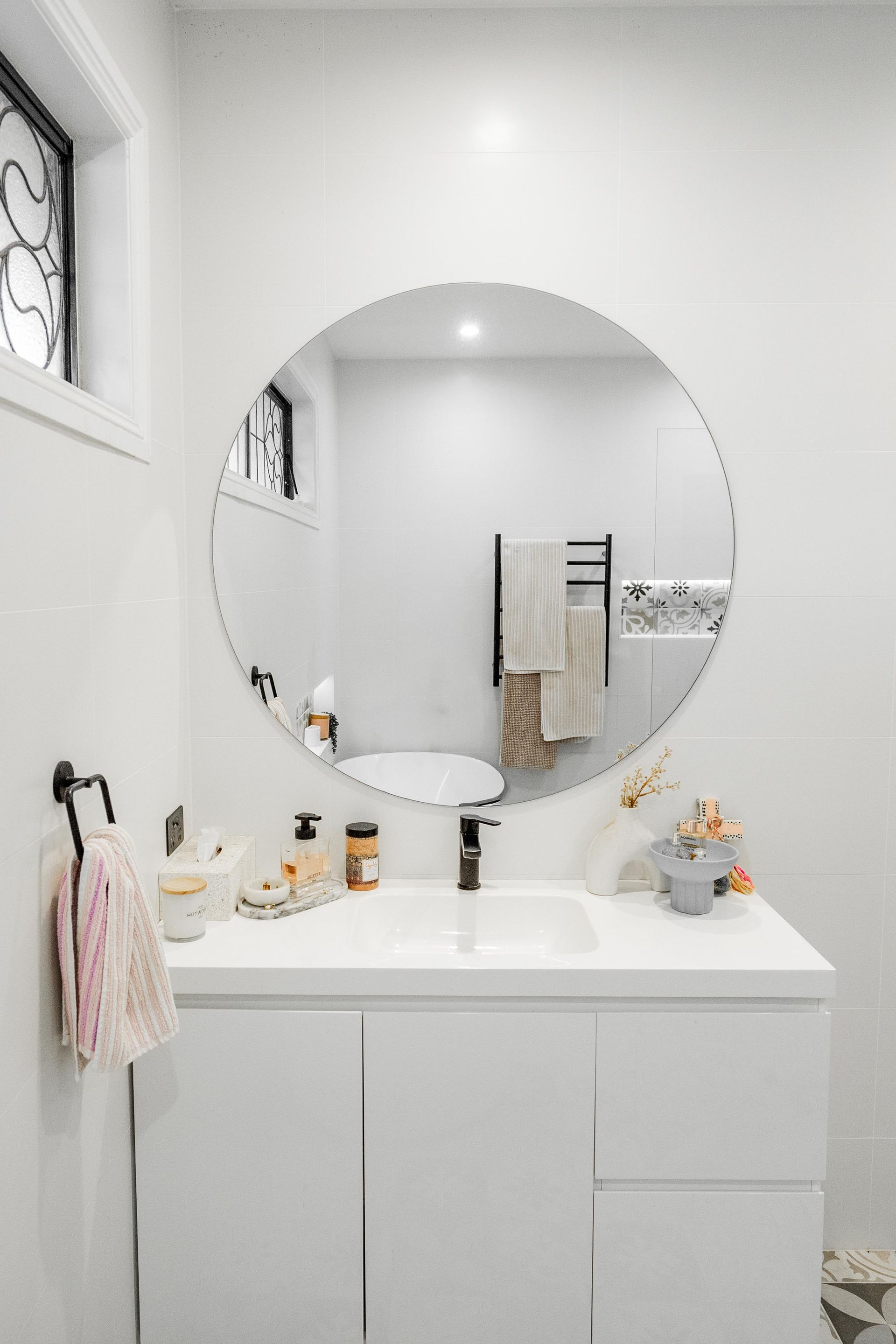 Bright white bathroom vanity with round mirror, sink, towels, and countertop decor — Cobra Plumbing & Bathrooms in Heathcote, NSW