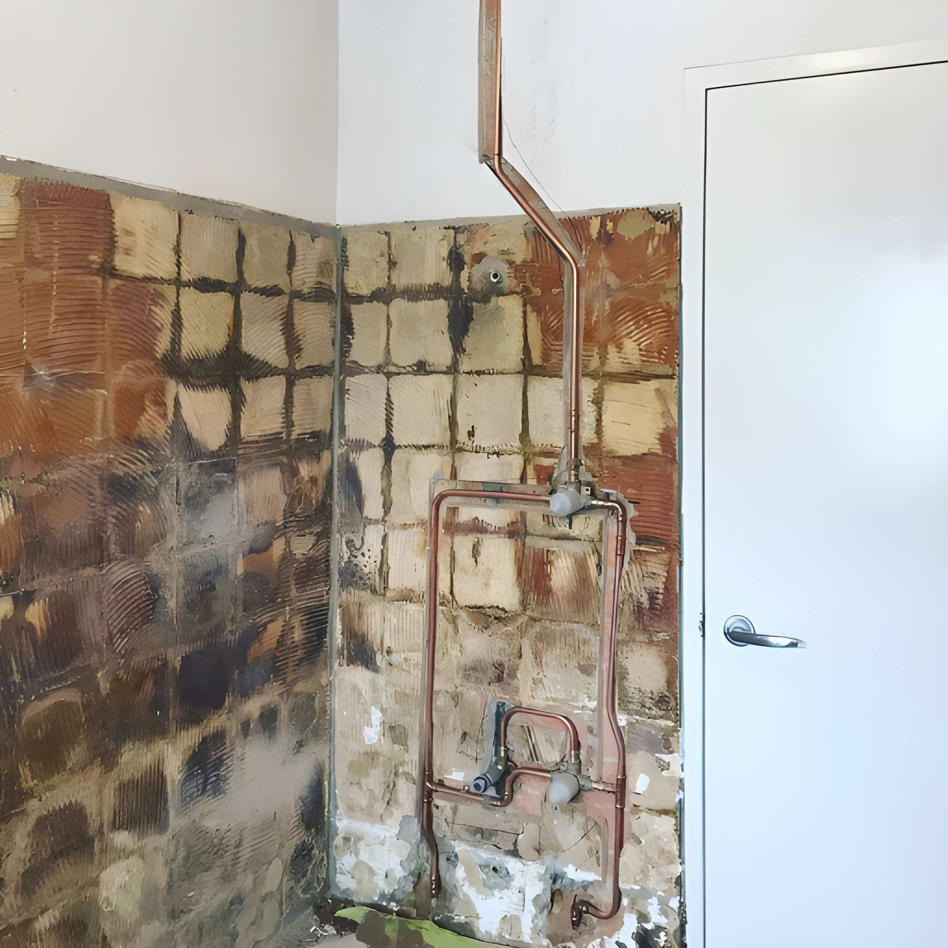 Copper Pipes on a Wall With Missing Tiles Next to a White Door — Cobra Plumbing & Bathrooms in Heathcote, NSW