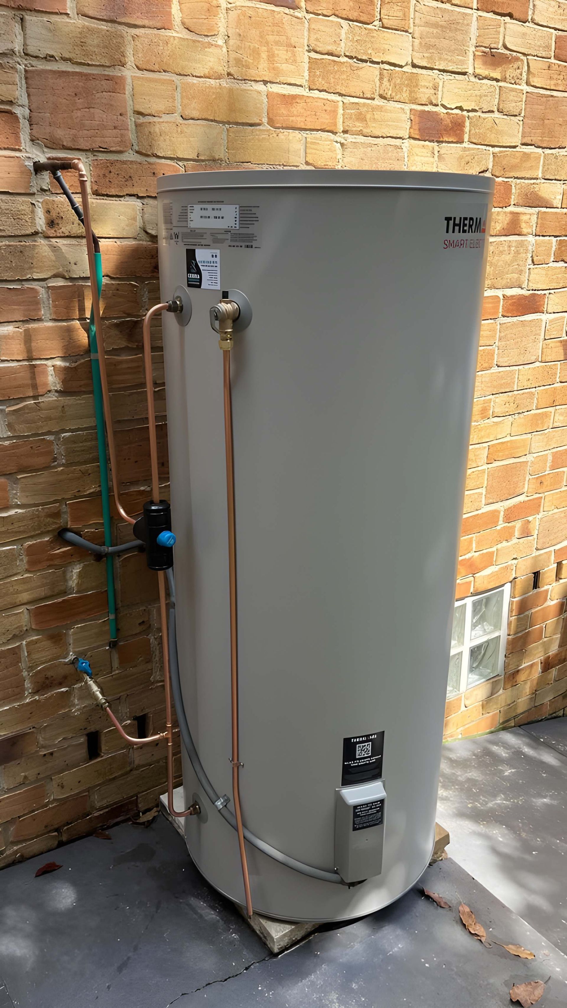 Tan Hot Water Tank Against a Brick Wall, With Copper and Green Pipes — Cobra Plumbing & Bathrooms in Heathcote, NSW
