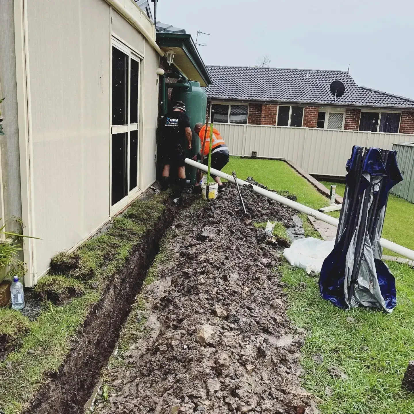 Workers Digging a Trench Beside a House — Cobra Plumbing & Bathrooms in Heathcote, NSW