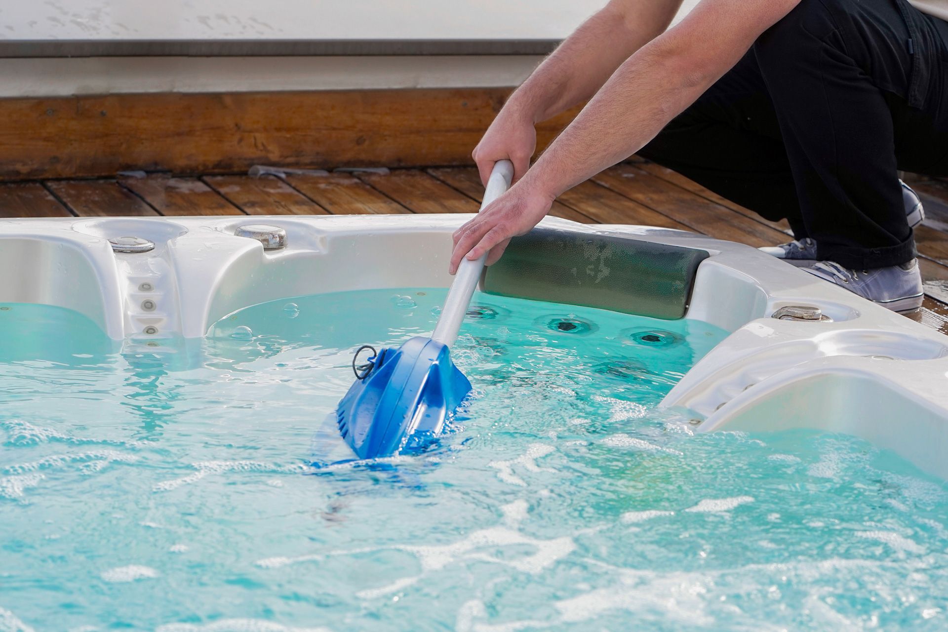 A person is cleaning a hot tub with a broom.