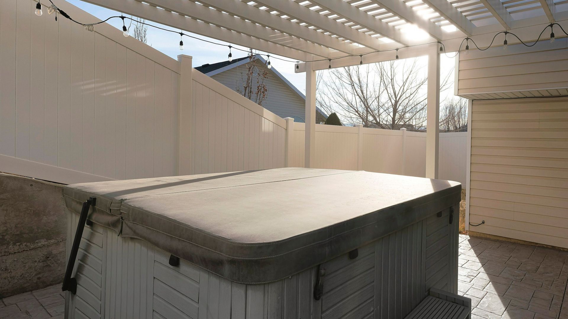 A hot tub under a pergola with a white fence in the background