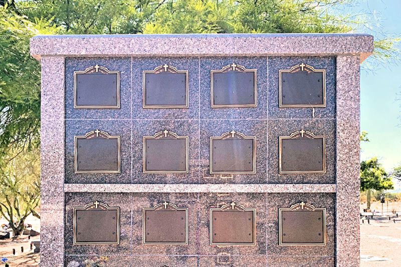 A granite columbarium with twelve bronze-framed memorial plaques arranged in three rows, set in an outdoor cemetery.