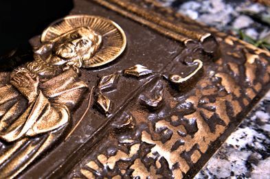 Bronze bas-relief of a haloed figure on a textured metal surface, set against a granite-like background.