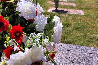 A close-up of a bouquet of red and white flowers resting on a granite headstone in a cemetery.