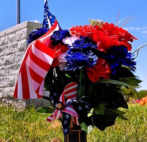 A bouquet of red, white, and blue flowers and a miniature American flag in a cemetery.