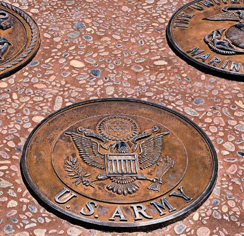 Three bronze-colored military service seals embedded in a textured concrete ground.