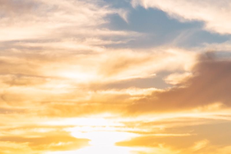 Soft golden sunlight glows behind wispy, layered clouds in a peaceful sunset sky.