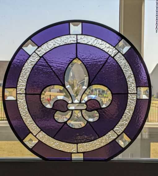 Purple circular stained-glass panel with a white fleur-de-lis design and geometric border
