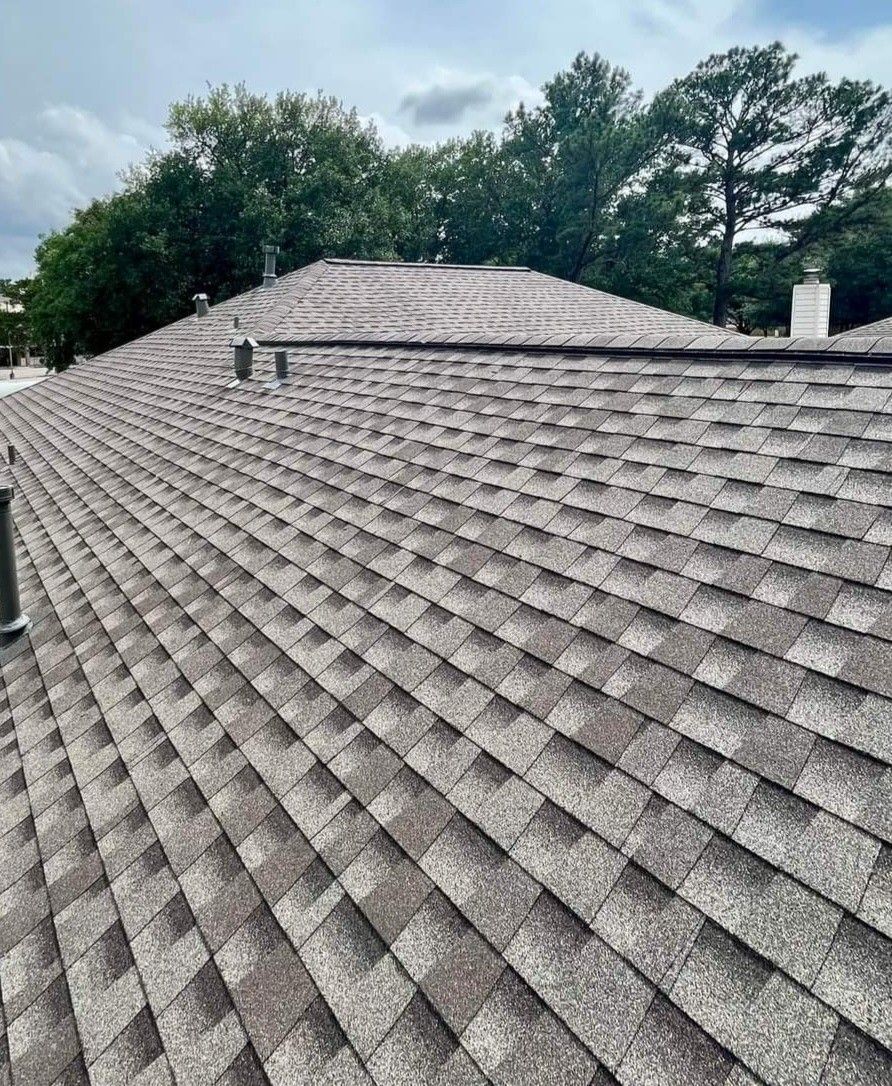 A close up of a roof with a chimney and trees in the background.