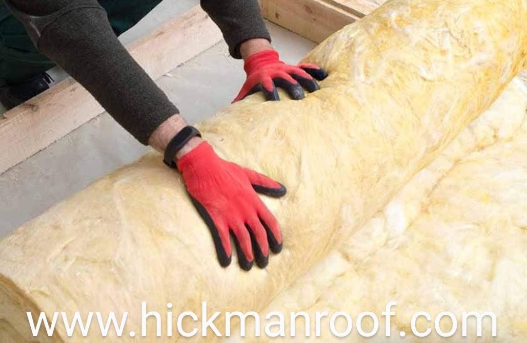 A person wearing red gloves is laying a piece of insulation on the floor.