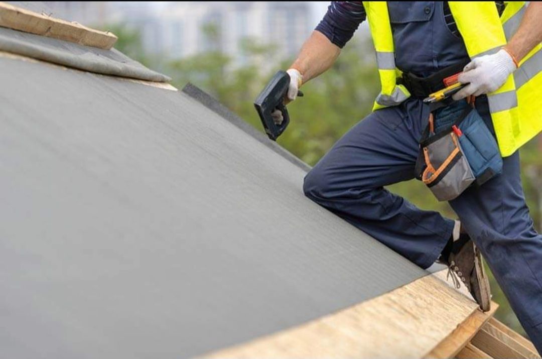 A man in a yellow vest is working on a roof.