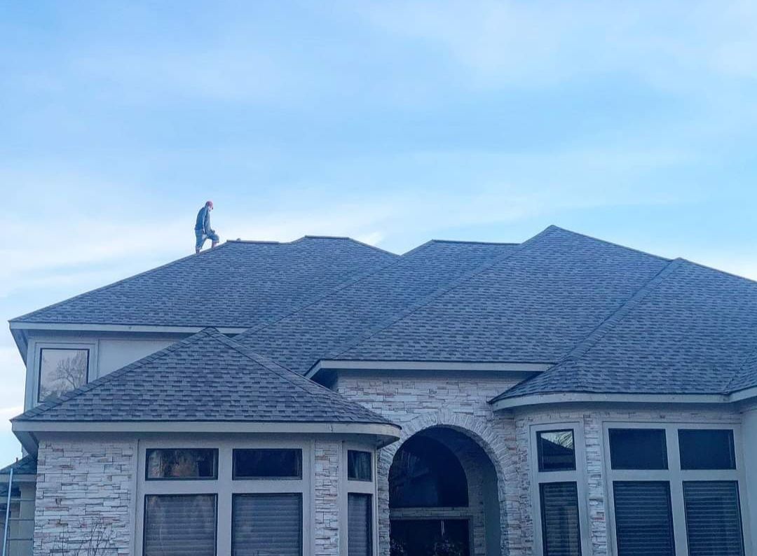 A man is standing on the roof of a large house.